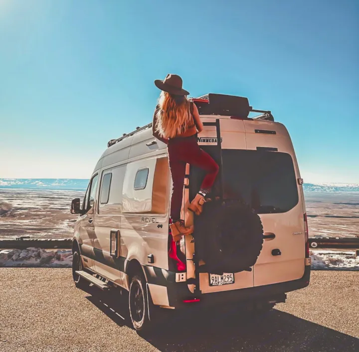 A traveler scales their RV rental van for panoramic views of snowy plains under a clear sky.. Winnebago Revel 2022