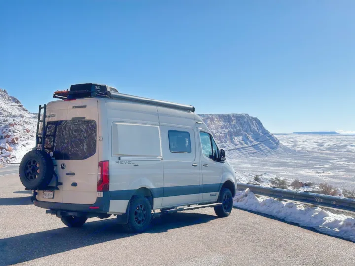 This RV rental camper van on a snowy mountain road offers expansive winter views. Perfect for a rugged road trip adventure.. Winnebago Revel 2022