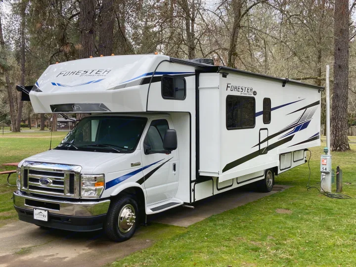 White Forest River Forester Class C rv rental parked at a tranquil campsite, connected to power with slide-out extended.. Forest River Forester 2023