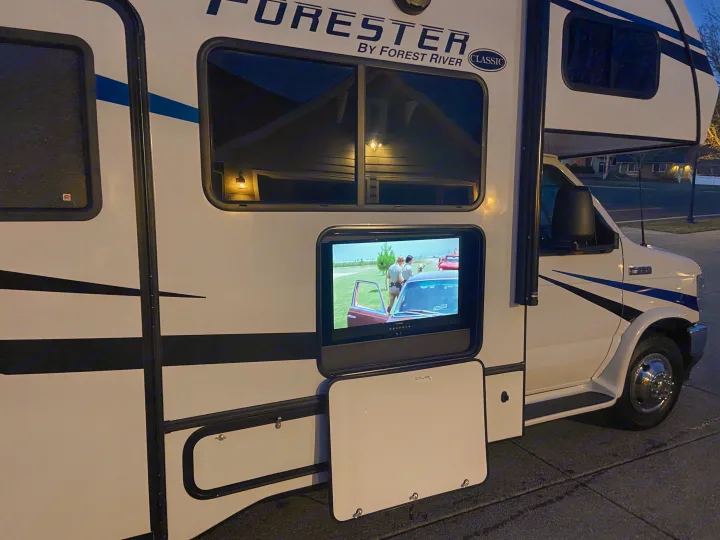 An RV rental features an outdoor TV showing a movie. Perfect for travel and camp entertainment.. Forest River Forester 2023
