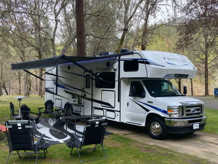 Forester RV rental parked at a lush campsite with outdoor living area, perfect for nature retreats.. Forest River Forester 2023