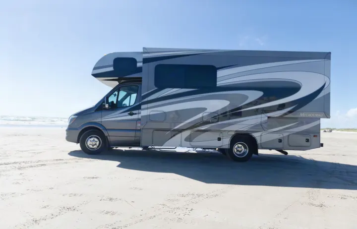 Grey RV rental on a sunny beach with ocean waves. Perfect for motorhome travel adventures by the sea!. Jayco Melbourne 2016