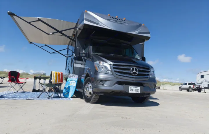 Mercedes-Benz Sprinter **rv rental** on a sunny beach with an extended awning, chairs, and boogie board for camping.. Jayco Melbourne 2016