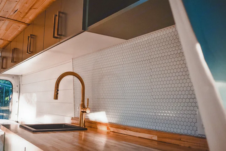 Inside a modern RV rental: well-appointed kitchen with a black sink, elegant gold faucet, and hexagon tile backsplash.. Ford Transit 2019