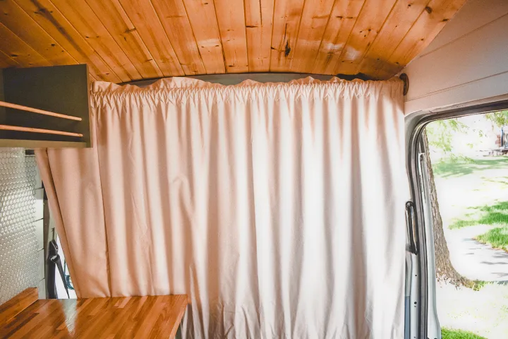Interior of an RV rental camper van with wood ceiling, a light privacy curtain across the cabin, and storage.. Ford Transit 2019