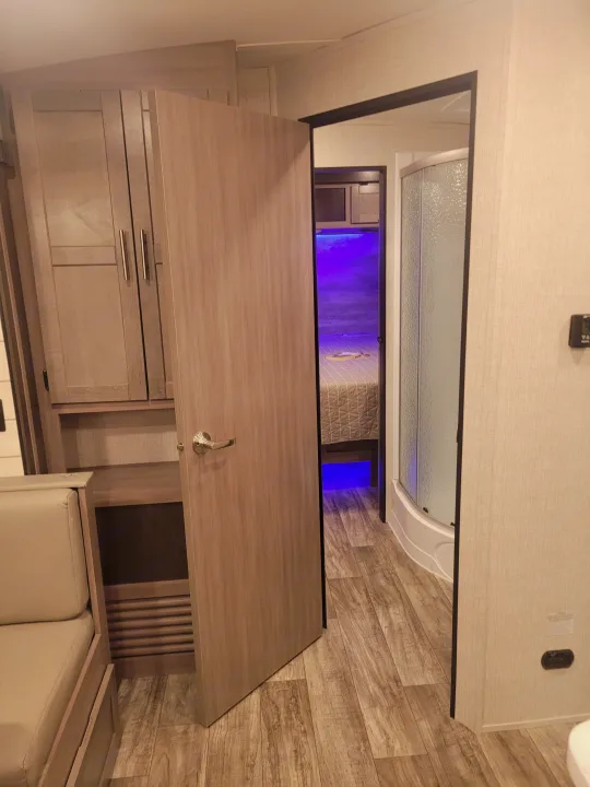 Open door inside an RV rental reveals a cozy bedroom with purple LED lighting and a compact shower, showcasing a functional layout.. Crossroads Sunset Trail 2023