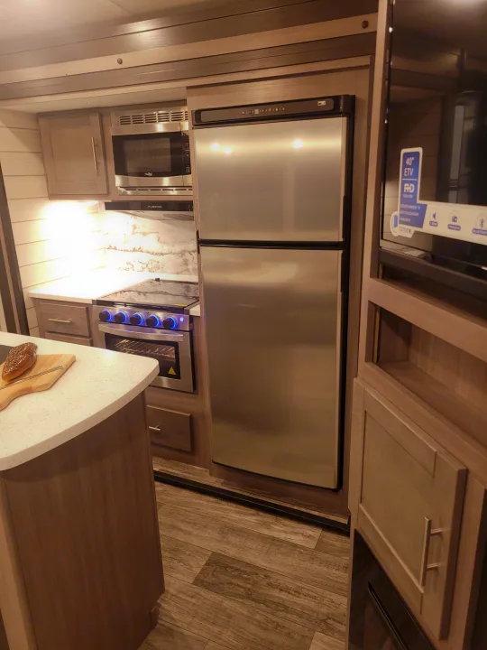 Modern RV rental kitchen showcasing a full-size fridge, microwave, and stove/oven setup.. Crossroads Sunset Trail 2023