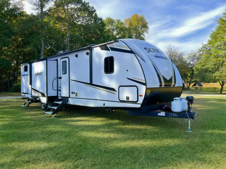 Spacious white rv rental travel trailer with an extended slide-out, parked on green grass. Perfect for your next camping adventure!. Crossroads Sunset Trail 2023