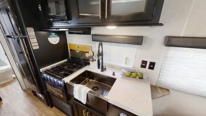 Inside an **rv rental**: a compact yet full-featured kitchen with a black fridge, stove, microwave, and stainless steel farmhouse sink.. Forest River Cherokee Grey Wolf Special Edition 2022