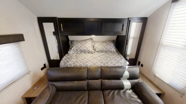 Cozy RV rental interior: a bed with patterned bedding, overhead cabinets, and a dark leather sofa in the foreground.. Forest River Cherokee Grey Wolf Special Edition 2022