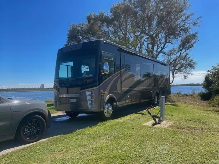 Our large RV rental offers a perfect lakeside retreat. This motorhome is set up at a scenic campsite under a clear blue sky.. Other Other 2021