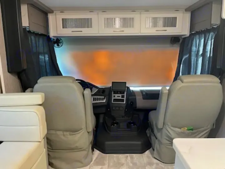 Inside this RV rental's cockpit, showing comfortable captain's chairs, dashboard, and overhead cabinets for an enjoyable journey.. Other Other 2021