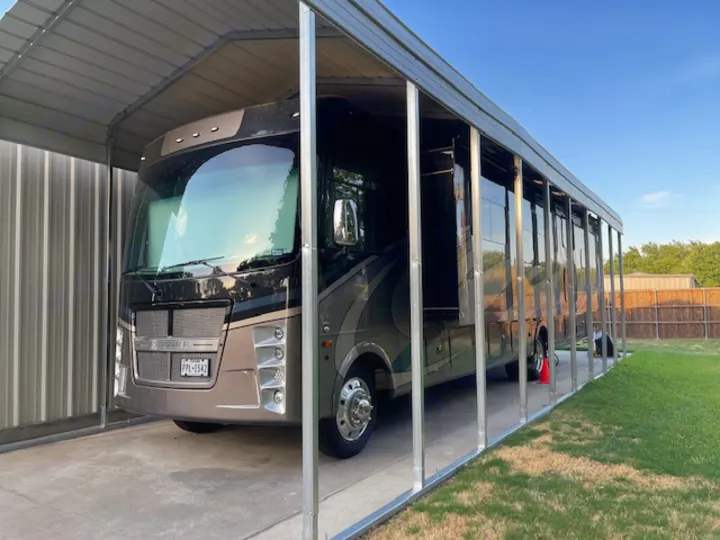 A spacious motorhome, perfect for an RV rental, is securely parked on a concrete pad under a new metal carport.. Other Other 2021