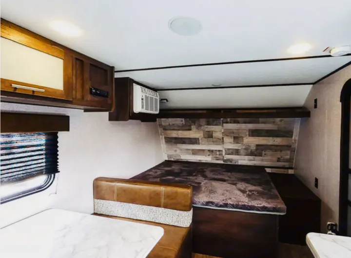 An inviting RV rental interior: dinette, convertible bed, overhead cabinets, and a rustic accent wall, perfect for comfortable travel.. Coleman Other 2021