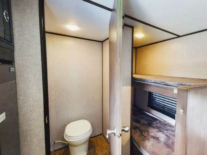 This RV rental features a compact bathroom with a toilet & cozy bunk beds, showing efficient travel trailer space.. Coleman Other 2021
