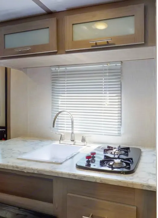 Modern RV rental kitchen showcasing light wood cabinets with frosted glass, a sink, countertop, and compact stovetop for convenience.. Coleman Other 2021