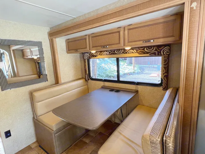 Cozy RV rental dinette with comfortable benches, a functional table, and overhead storage, perfect for meals on the go.. Thor Vegas 2016