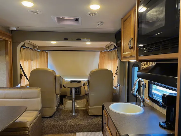 Inside a clean RV rental. View from rear showing kitchen, dinette, and front cockpit area with swivel seats.. Thor Vegas 2016