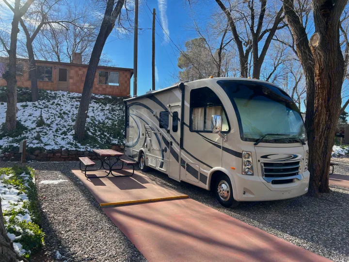 Cream RV rental parked at a snowy campsite with a picnic table and bare trees under a clear blue sky.. Thor Vegas 2016