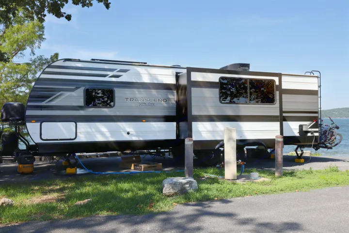 Lakeside RV rental travel trailer at a sunny campground. This Transcend Xplor is set up for camping with bikes and hookups.. Grand Design Transcend Xplor 2022