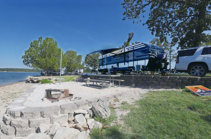 RV rental by a tranquil lake campsite featuring a picnic area, fire pit, and cornhole game.. Grand Design Transcend Xplor 2022