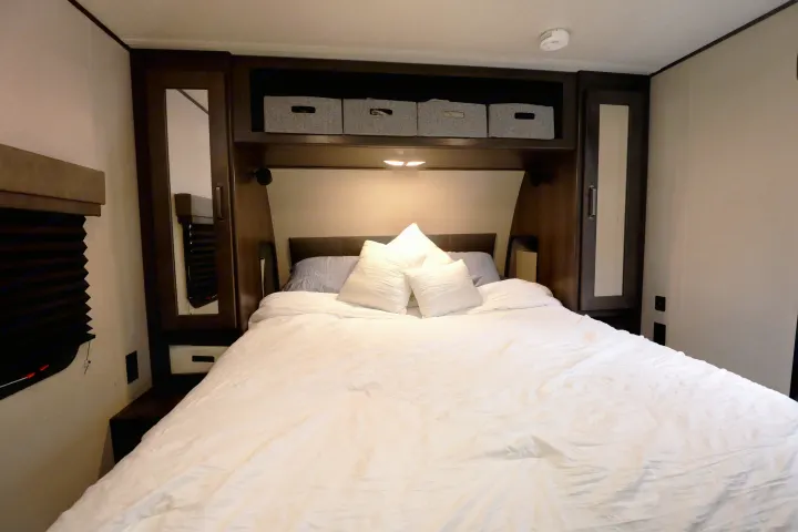 Spacious RV rental bedroom featuring a large bed with white linens, overhead storage, and mirrored cabinets for a comfortable stay.. Grand Design Transcend Xplor 2022