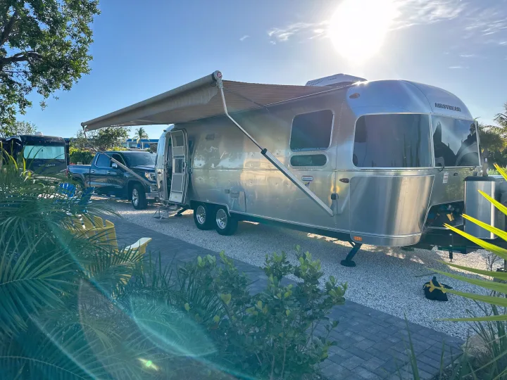 A classic Airstream rv rental travel trailer, with its awning extended for shade, parked on a sunny day with a pickup truck nearby.. Airstream International 2020