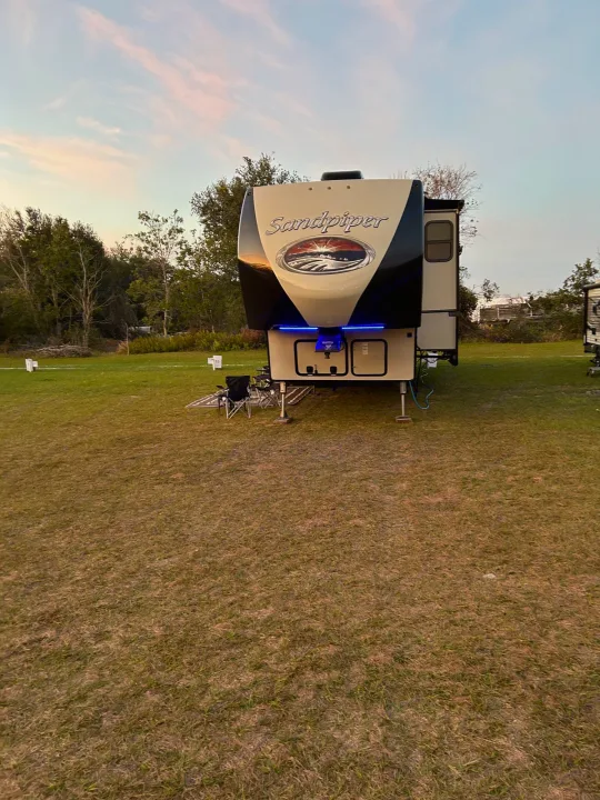 A large white and black Sandpiper fifth-wheel RV is parked on a grassy campsite at dusk, with blue lights. Perfect for an RV rental getaway.. Forest River Sandpiper 2018