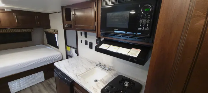 This RV rental interior offers a cozy bed and a fully equipped kitchen with a microwave, stovetop, and sink.. Jayco Jay Flight SLX 184 BS 2019