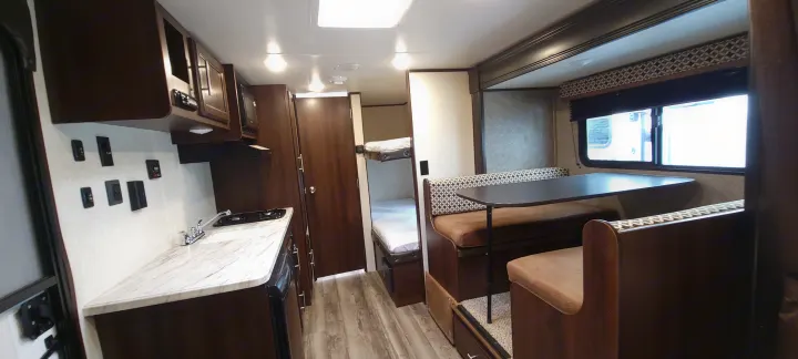 Modern RV rental interior with dark wood cabinets, a full kitchenette, a cozy dinette, and private bunk beds.. Jayco Jay Flight SLX 184 BS 2019