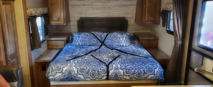Cozy RV rental bedroom features a patterned bed secured with straps, side tables, & storage cabinets.. Forest River Flagstaff Micro Lite 2018