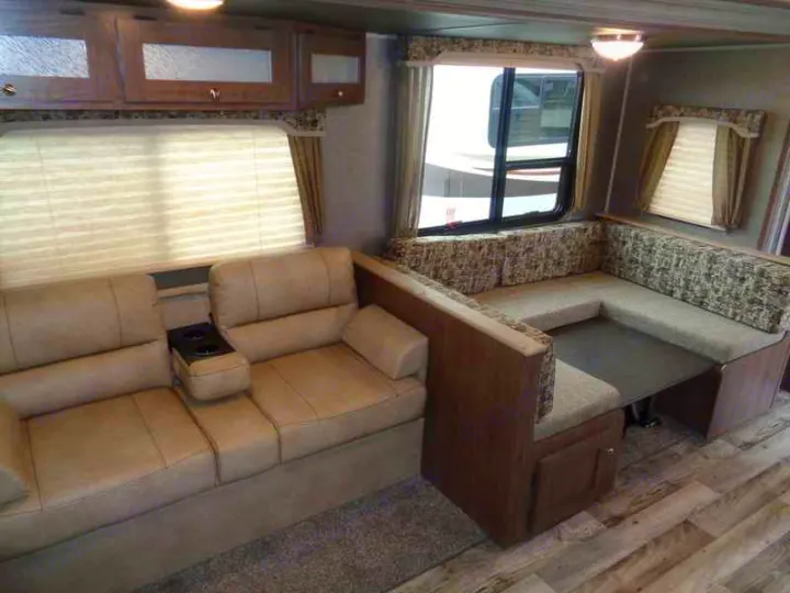 Inside this rv rental: a tan sofa with cupholders, wooden cabinets, and a U-shaped dinette with a table.. Keystone RV Hideout 2018