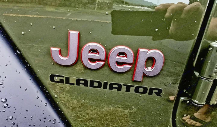 Wet Jeep Gladiator truck body & emblems, with reflections of sky & a foot. Perfect for an RV rental getaway.. Jeep Gladiator Rubicon 2023