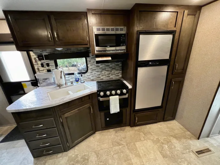 Well-equipped RV rental kitchen: dark wood cabinets, stainless steel appliances, double sink, and generous counter space.. Jayco Jay Flight SLX 2020