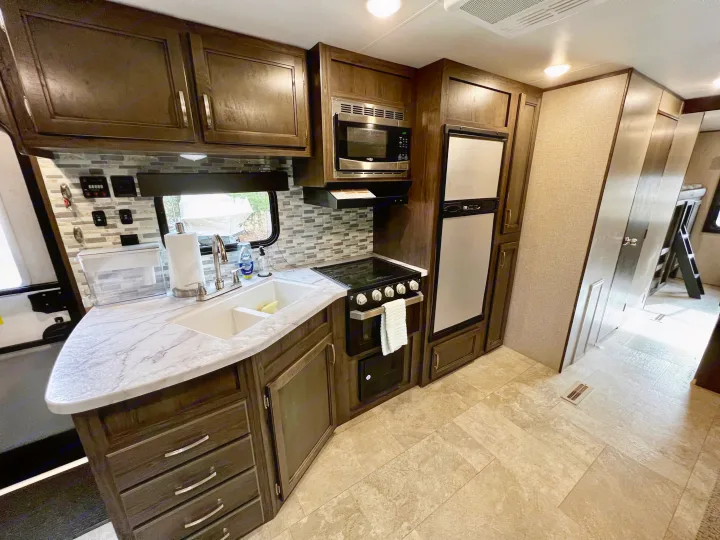This RV rental features a well-equipped kitchen with dark wood cabinets, a microwave, stove, sink, and refrigerator.. Jayco Jay Flight SLX 2020