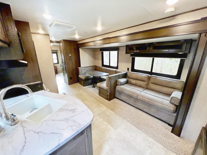 Bright RV rental interior: kitchen with marbled counter and sink, dinette, and comfy sofa in a neutral color scheme.. Jayco Jay Flight SLX 2020