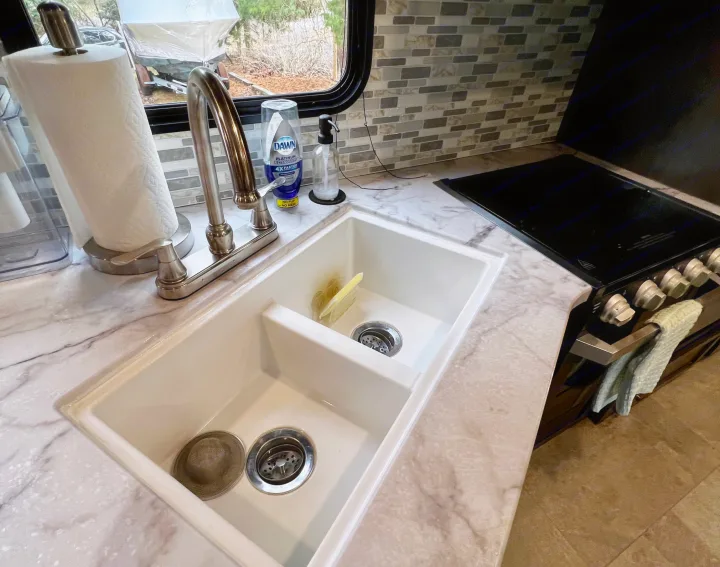 Clean RV rental kitchen featuring a double sink, modern faucet, electric stovetop, and marble-look counters. Paper towels & soap visible.. Jayco Jay Flight SLX 2020