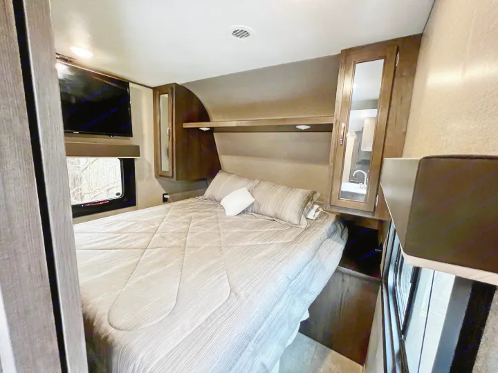 Relax in this RV rental bedroom featuring a comfortable bed, wall-mounted TV, window, and built-in storage.. Jayco Jay Flight SLX 2020