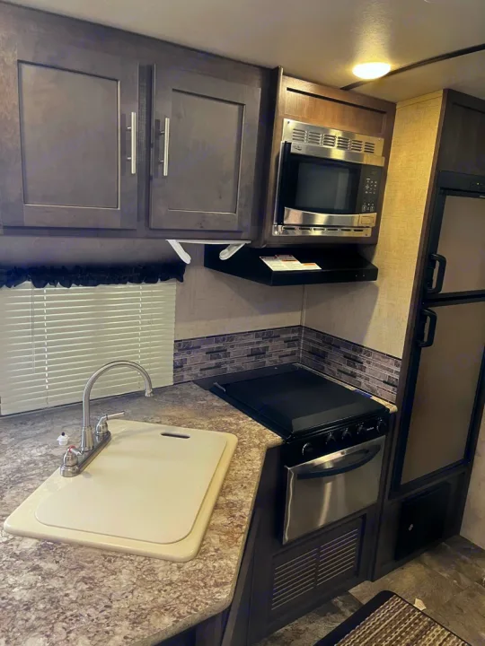 A modern RV rental kitchen, equipped with a sink, stainless steel microwave, stove/oven, and fridge for your travels.. Forest River Surveyor 2016