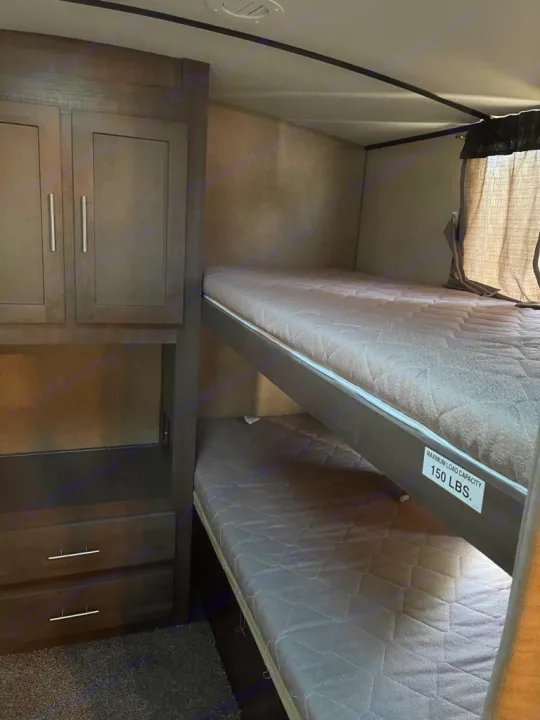 This RV rental features two stacked bunk beds with quilted mattresses and dark wood storage, showing a 150lb weight limit.. Forest River Surveyor 2016