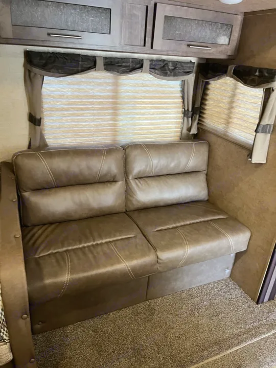 Inside an RV rental: a plush brown sofa, overhead cabinets, and windows with blinds for road trip comfort.. Forest River Surveyor 2016