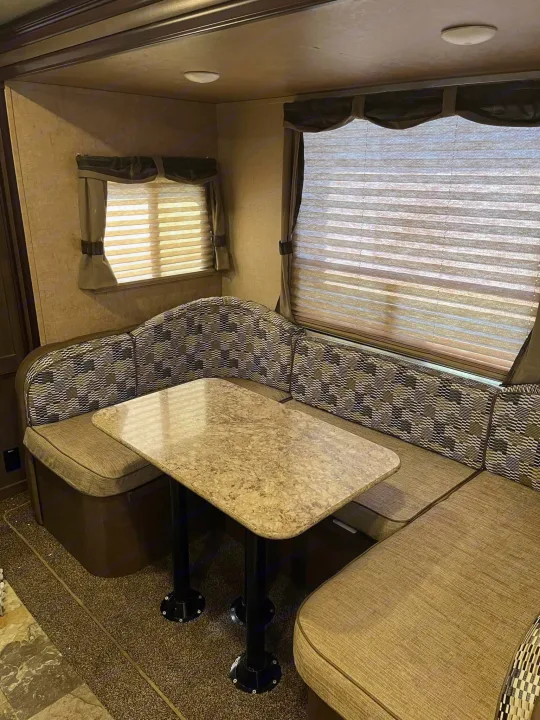 This RV rental features a cozy dinette with a U-shaped bench, table, and large windows with blinds, offering warm interior light.. Forest River Surveyor 2016