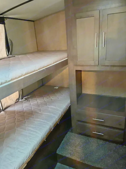 RV rental interior featuring two bunk beds with mattresses, alongside a dark wood storage unit with cabinets and drawers.. Forest River Surveyor 2016