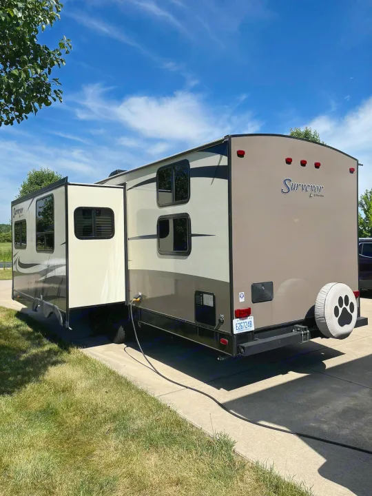 Tan and brown RV rental, a Surveyor travel trailer with extended slide-out and unique paw print tire cover, ideal for trips.. Forest River Surveyor 2016