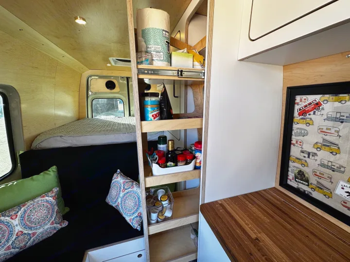 Cozy RV rental interior with wooden paneling, smart storage shelves for food & supplies, a comfy bed, and built-in kitchen space.. VanCraft VanCraft Class B 2022
