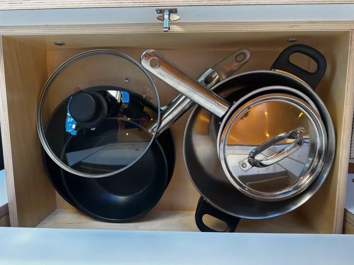 Neatly organized pots, pans, and lids in a compact wooden RV rental compartment. Essential kitchenware.. VanCraft VanCraft Class B 2022