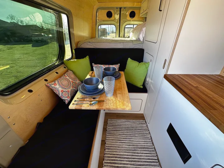 Cozy RV rental interior with a dining table set, comfortable seating, and a bed in the background for mobile living.. VanCraft VanCraft Class B 2022