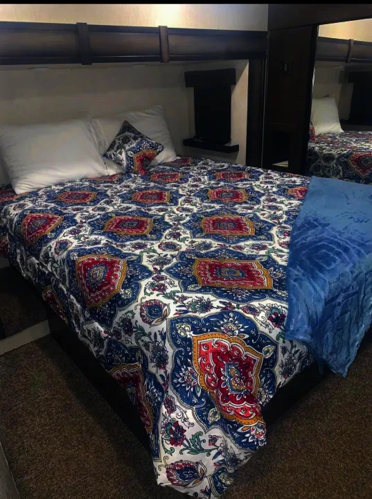 Cozy RV rental bedroom with a colorful duvet, plush pillows, and a soft blue throw, inviting for travel comfort.. Heartland Elkridge 2019