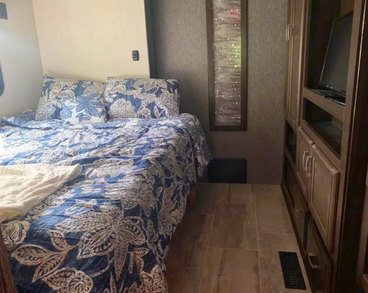 Cozy RV rental bedroom featuring floral bedding, a mounted TV, and built-in storage for comfortable travel.. Heartland Elkridge 2019
