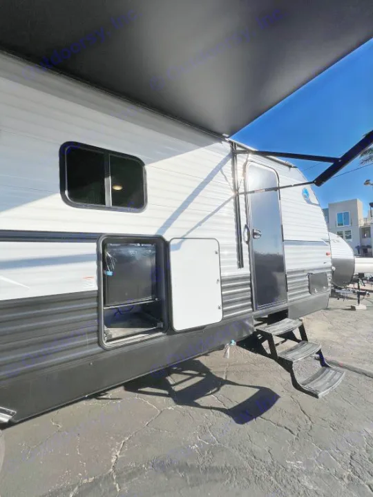 Side view of a modern RV rental, featuring an extended black awning and open exterior storage compartments, parked on asphalt.. Coachmen Clipper 262 BH C 2023